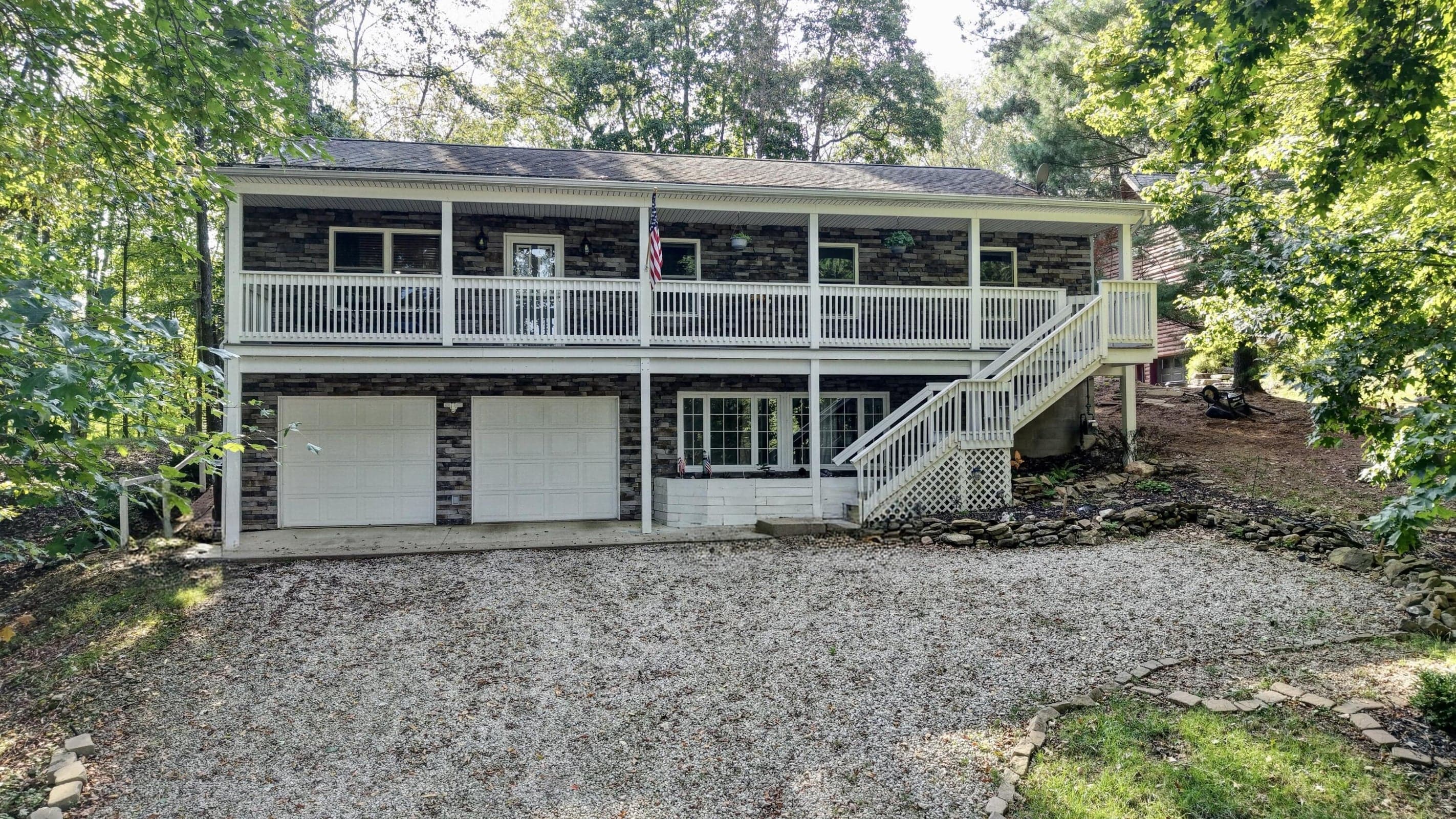 Stone veneer exterior with a two-car garage, upper-level balcony, and exterior staircase