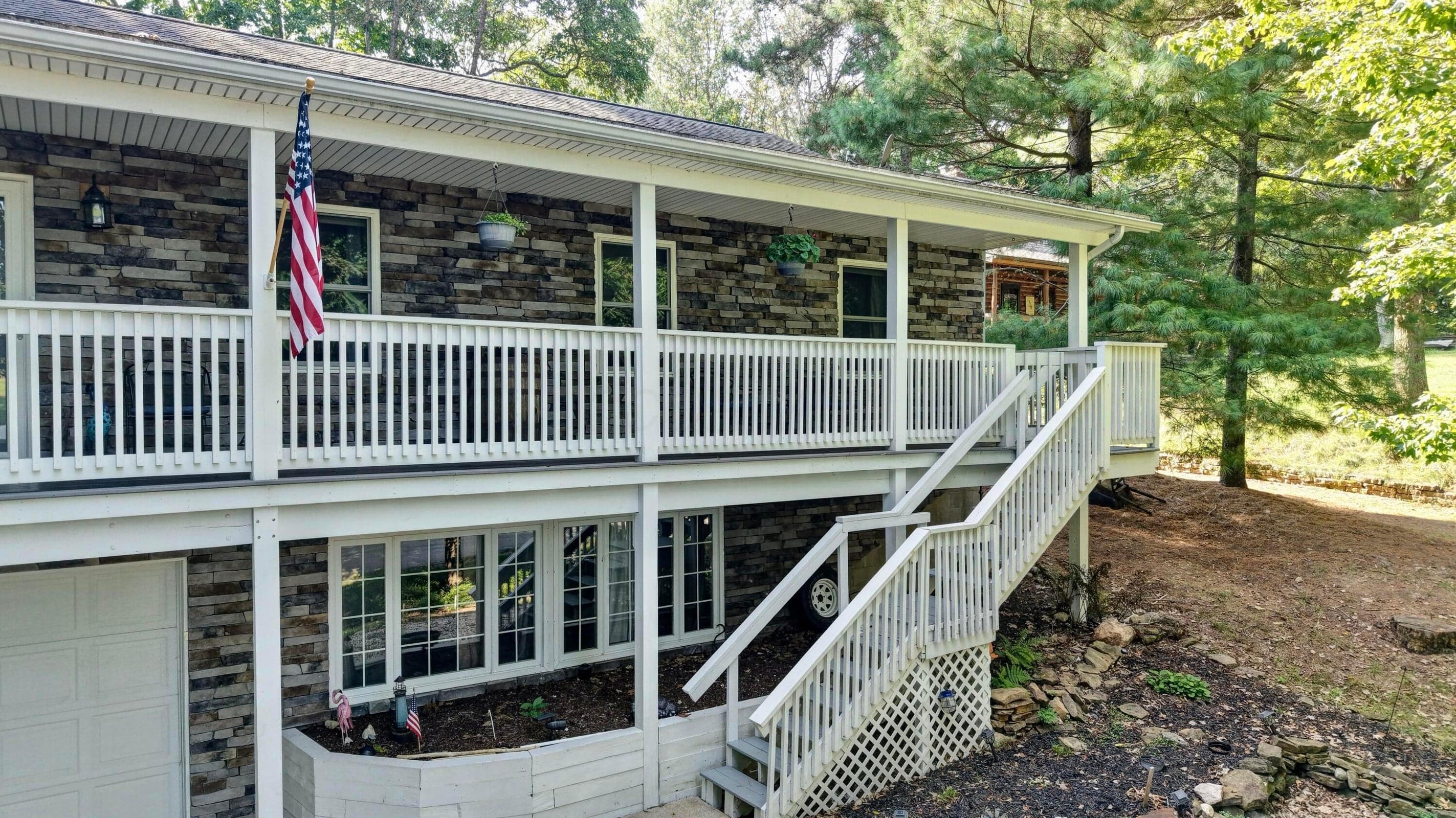 Stone veneer exterior with a full-length covered porch, white railing, and a multi-level staircase