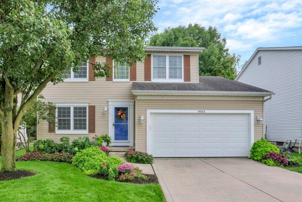 Two-story home featuring light beige siding, brown window shutters, an attached two-car garage, and a blue front entry door