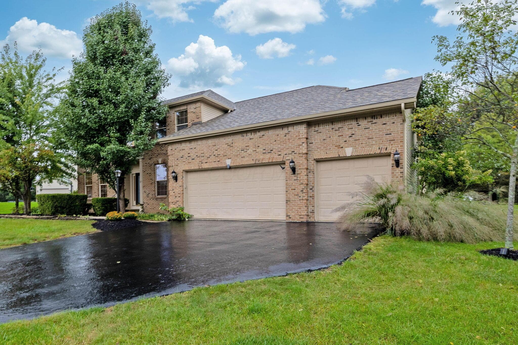 Brick exterior with multiple windows, two garage doors, and an asphalt driveway