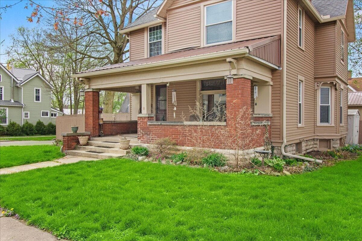 Expansive front yard with a walkway, covered front porch, brick columns, and a landscaped garden bed