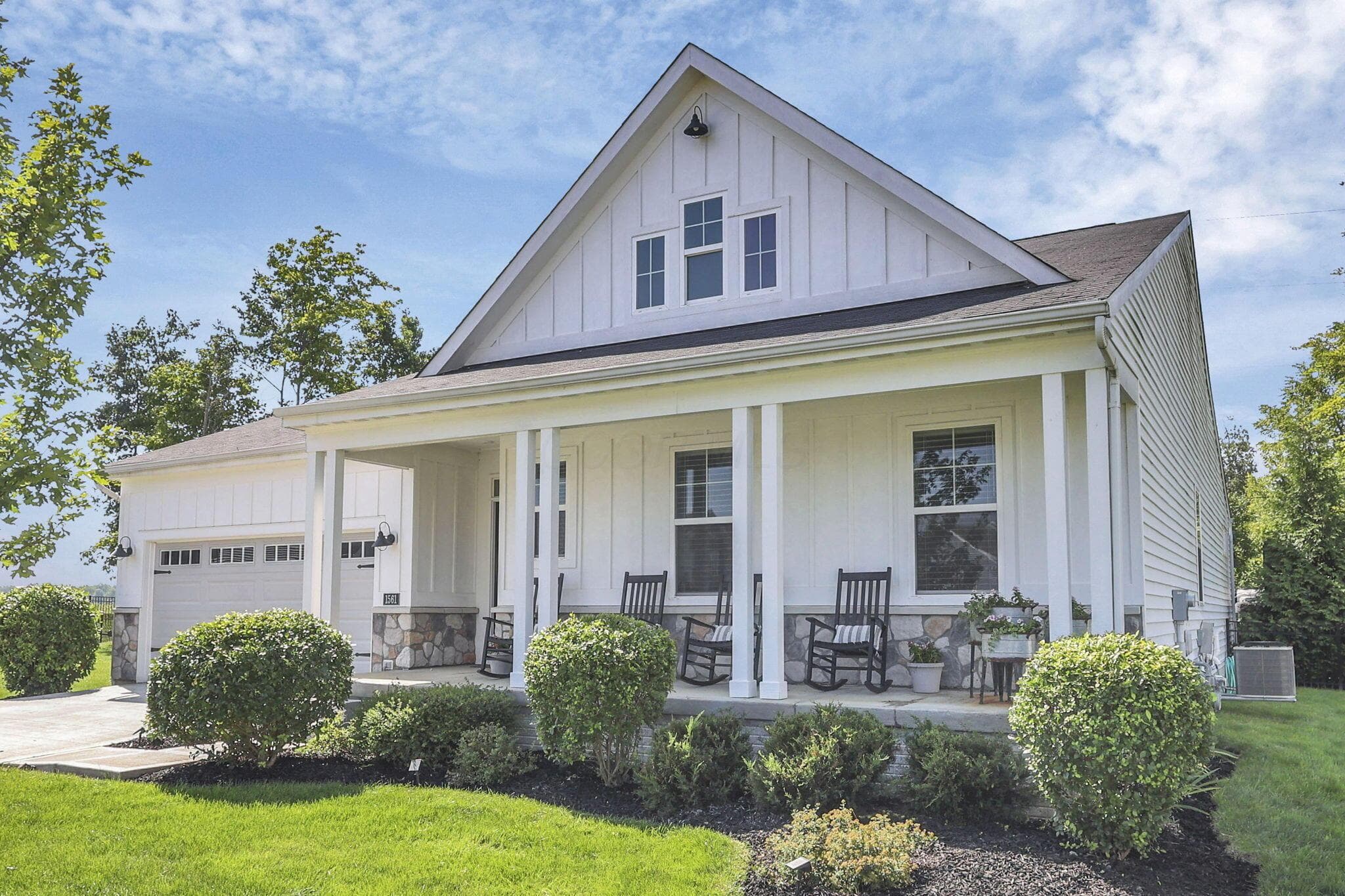 White board and batten siding, stone facade accents, covered front porch, gabled roofline, and attached garage