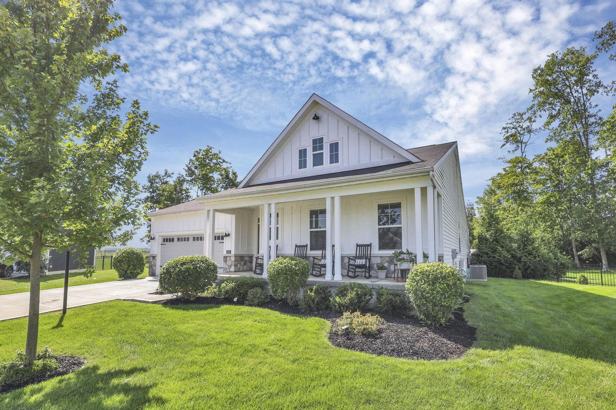 White siding exterior with a prominent gabled roofline, covered front porch, stone column bases, and a paved driveway leading to an attached garage
