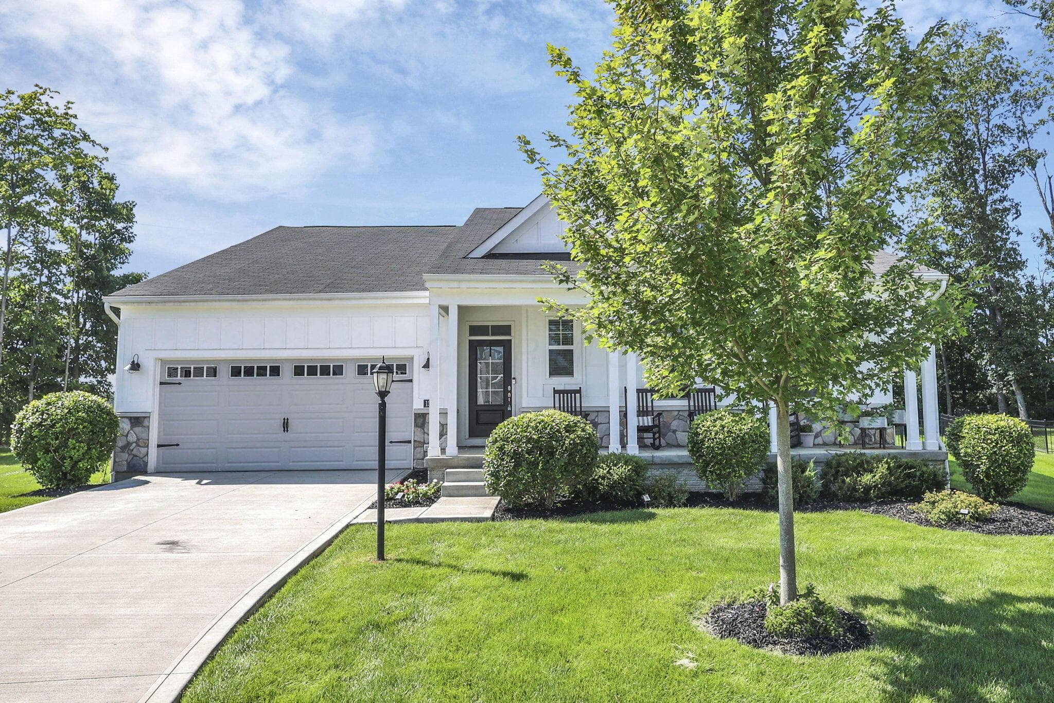 White siding exterior with a dark shingle roof, stone accent columns, attached two-car garage, and a covered front porch