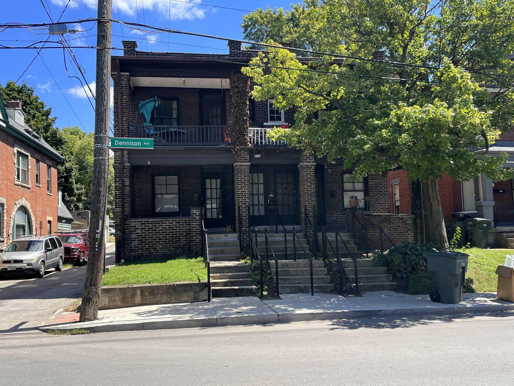 Brick facade with multiple entrances, concrete steps with metal railings, upper-level balconies, and mature landscaping
