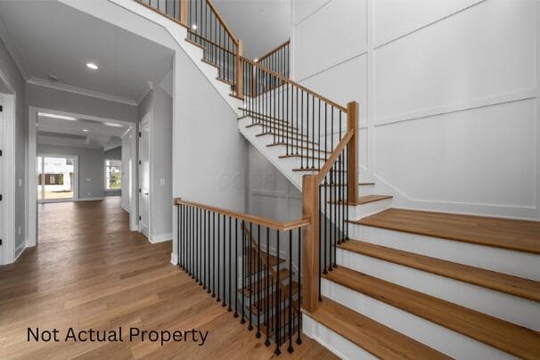 Wood-finish flooring throughout, board and batten wall detailing, staircase with natural wood handrails and black metal balusters, recessed lighting, and crown molding