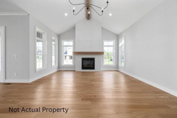 Vaulted ceiling with an exposed beam, a fireplace with a wood mantel, wood-finish flooring, and multiple windows with white trim