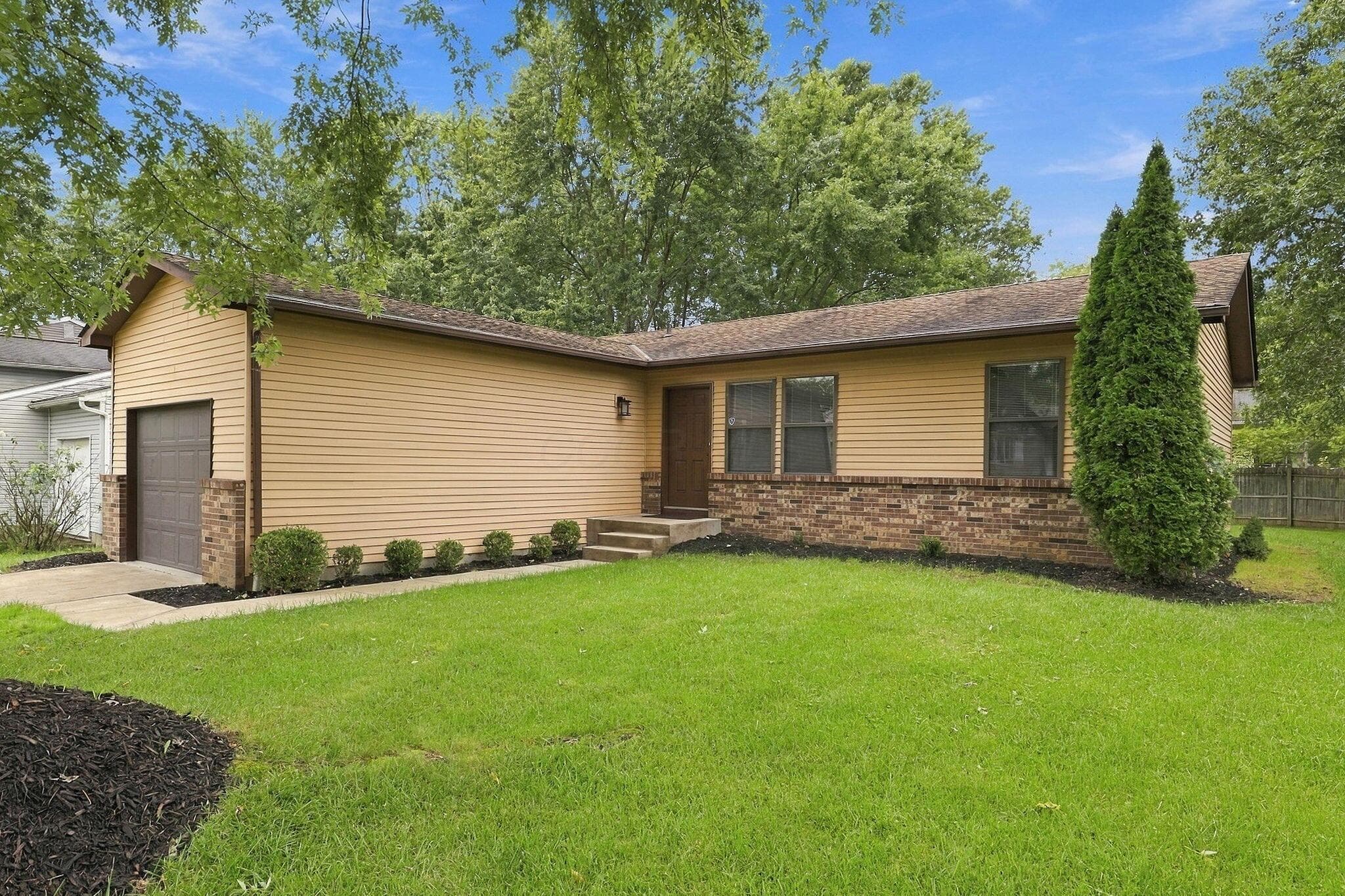 Single-story residence featuring light-colored siding, a dark brick foundation, and an attached garage with a panel door.