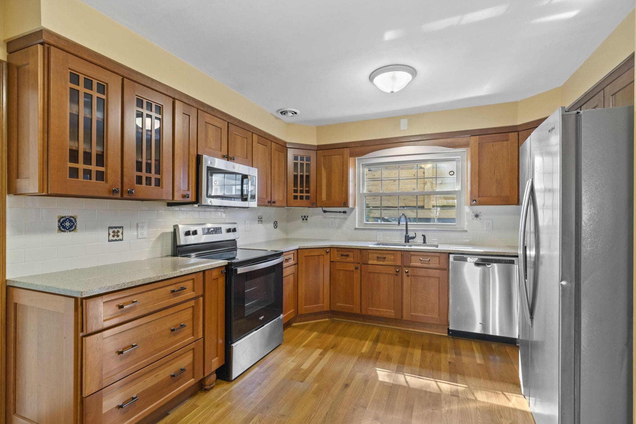 Kitchen featuring wood cabinetry, stainless steel appliances, light-toned countertops, tile backsplash, and wood-finish flooring