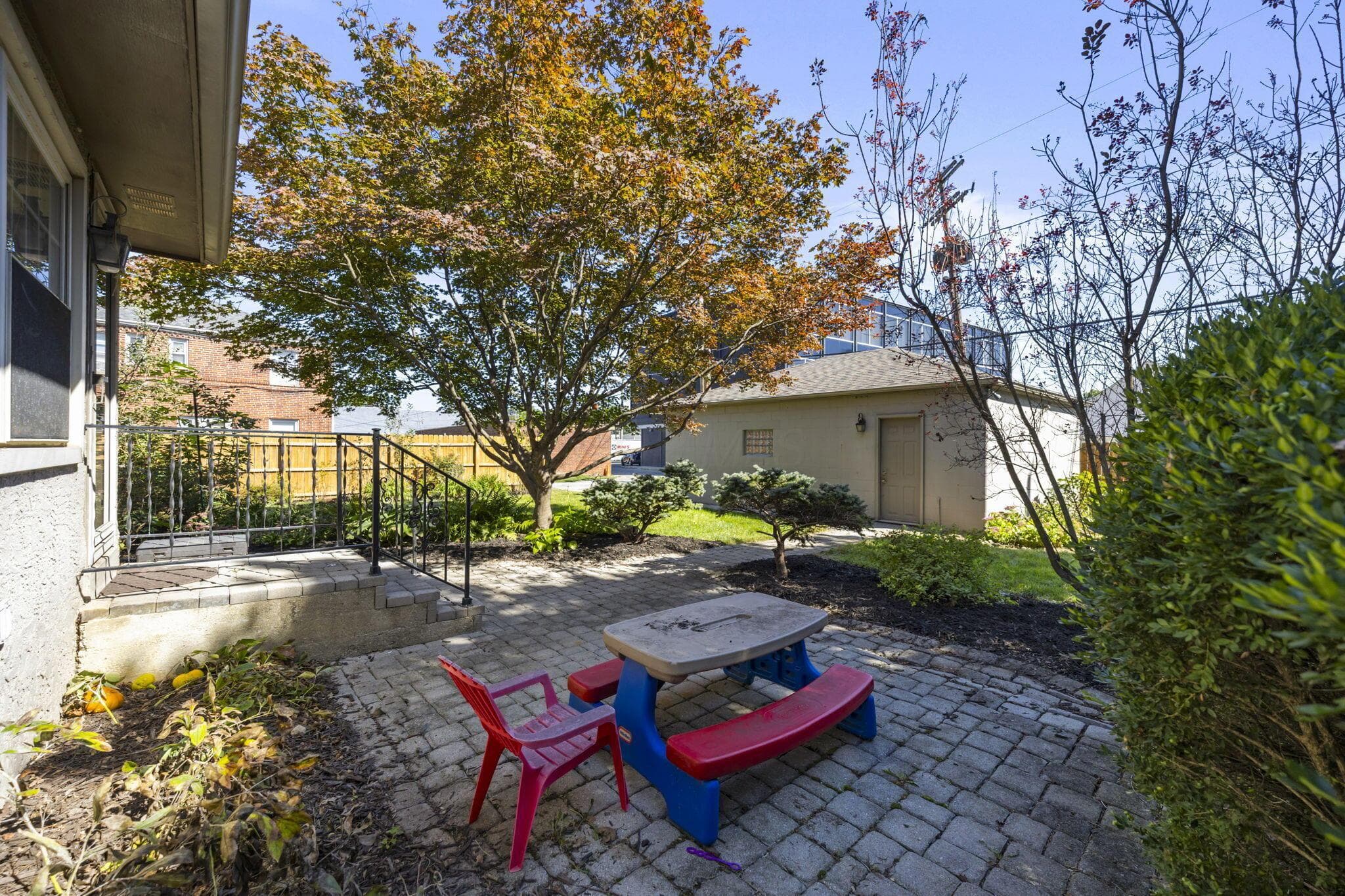 Paved patio area, mature tree, established shrubbery, stone steps, metal handrails