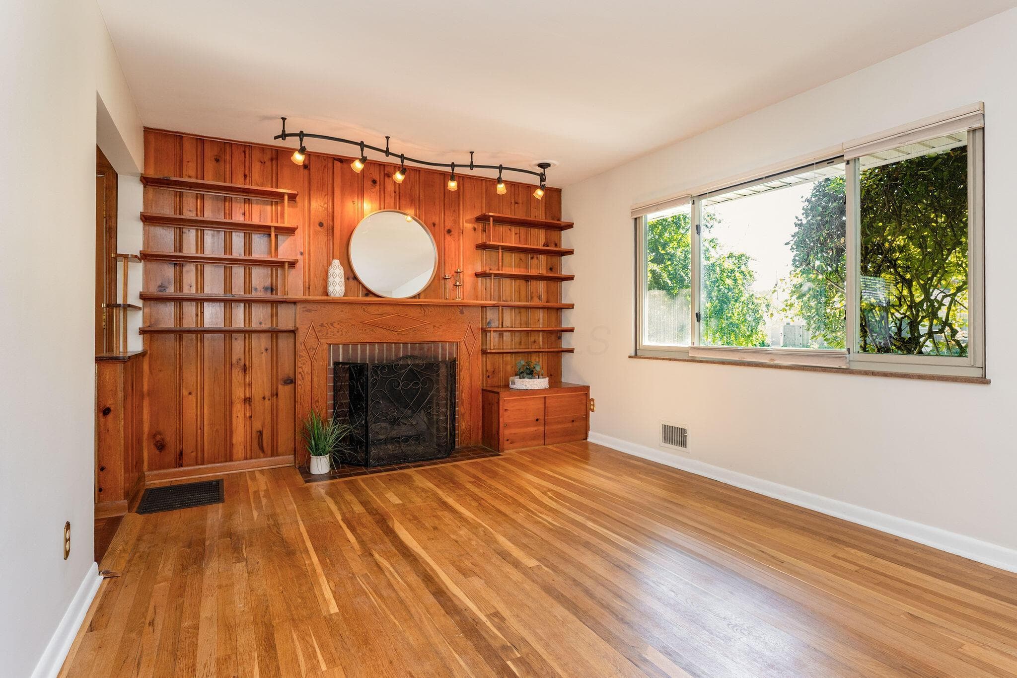 Step inside to the generous living room with hardwood flooring, a beautiful wood-paneled accent wall, built-in shelving, gas log fireplace with black metal screen, and large horizontal picture window.