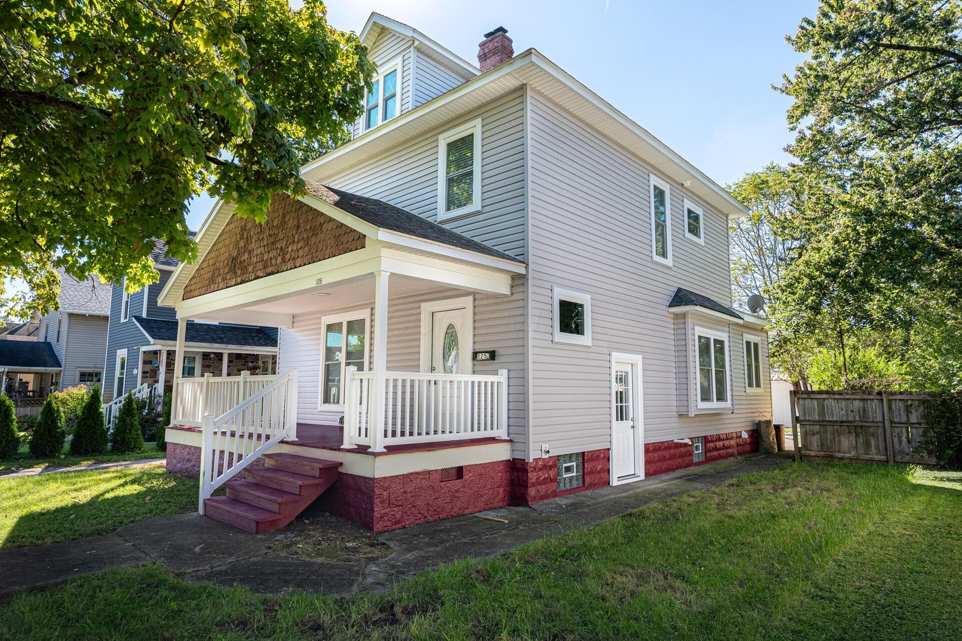 Two-story residence featuring light gray siding with white trim, a covered front porch with white railing, and a bay window
