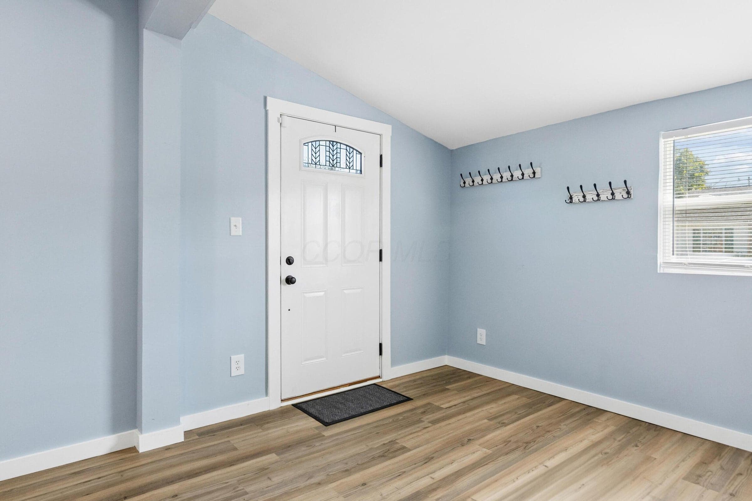 White front door with decorative glass insert, wood-finish flooring, and natural light from the window