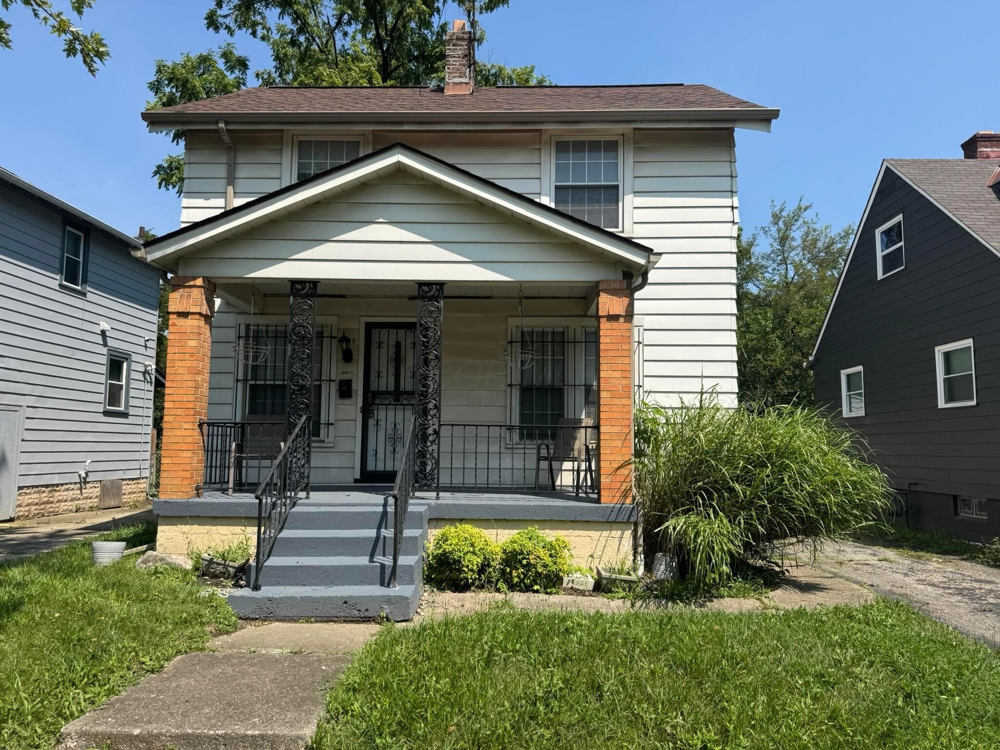 Two-story residence featuring siding exterior, covered front porch with brick columns, and a paved driveway