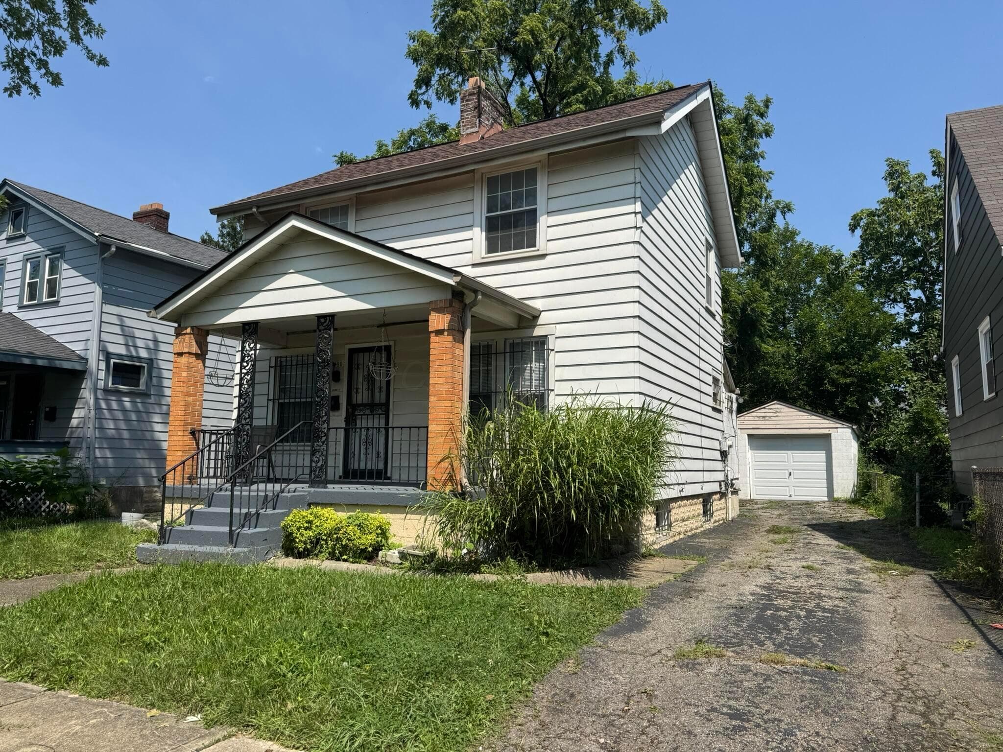 Two-story residence featuring horizontal siding, a covered porch with brick columns, and an asphalt driveway leading to a detached garage