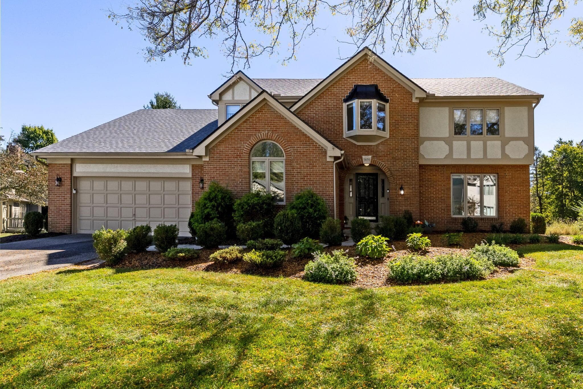 Brick facade with stucco accents, an attached two-car garage, a bay window, and a prominent arched entryway