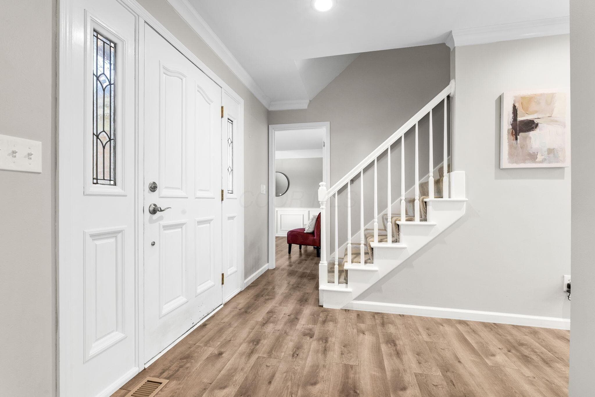 Entryway featuring wood-finish flooring, a white paneled front door with decorative glass sidelites, and a staircase with white balusters