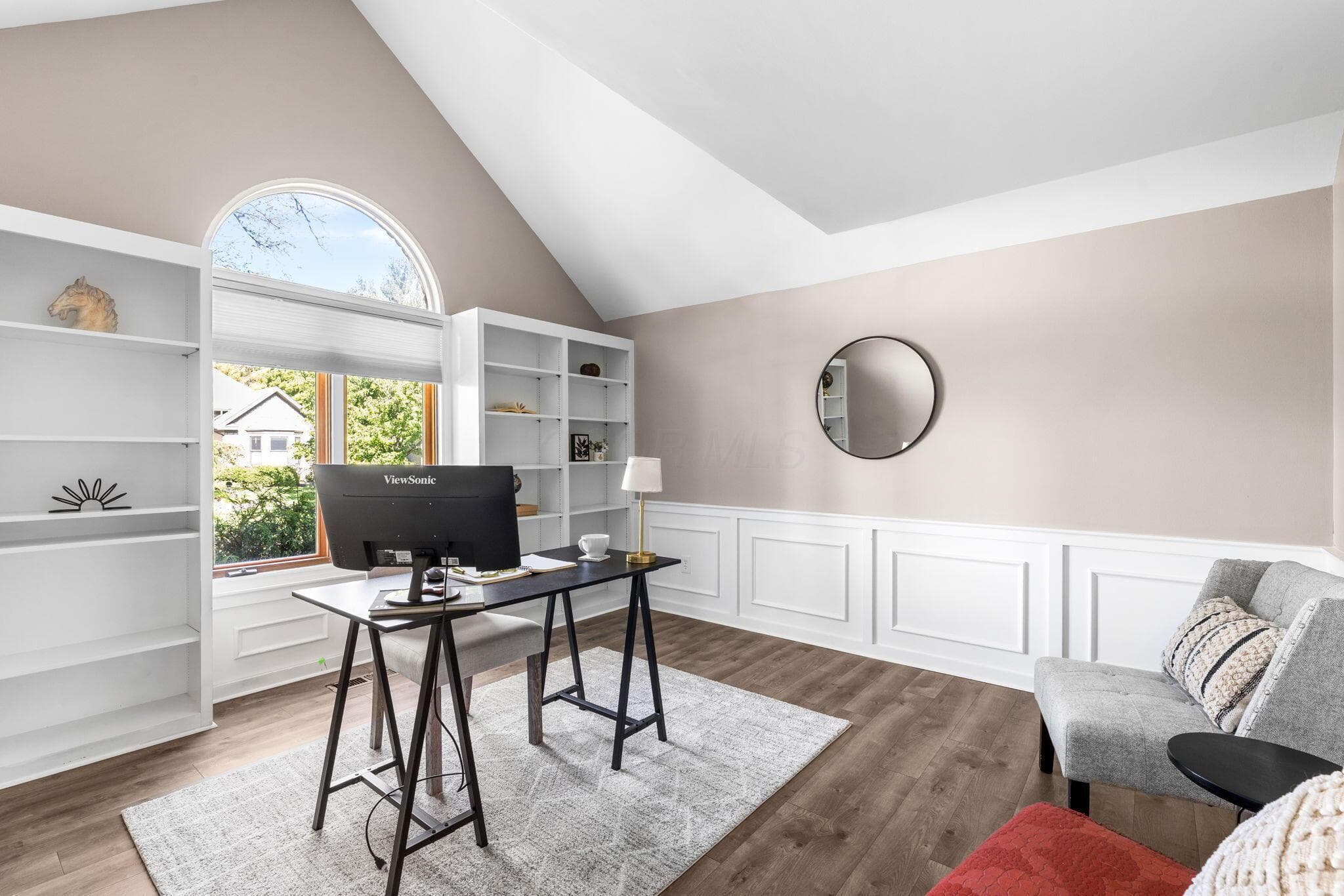 Vaulted ceiling, built-in shelving, arched transom window, wood-finish flooring, and decorative wainscoting