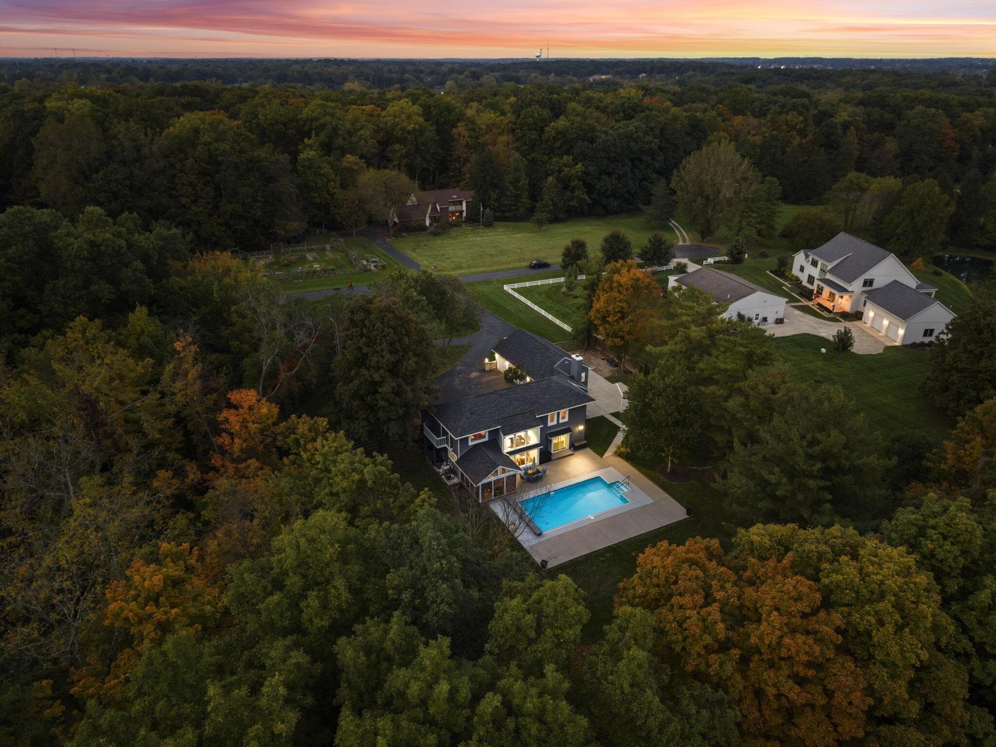 Wooded lot with a dark-sided residence, a rectangular swimming pool, and concrete hardscaping