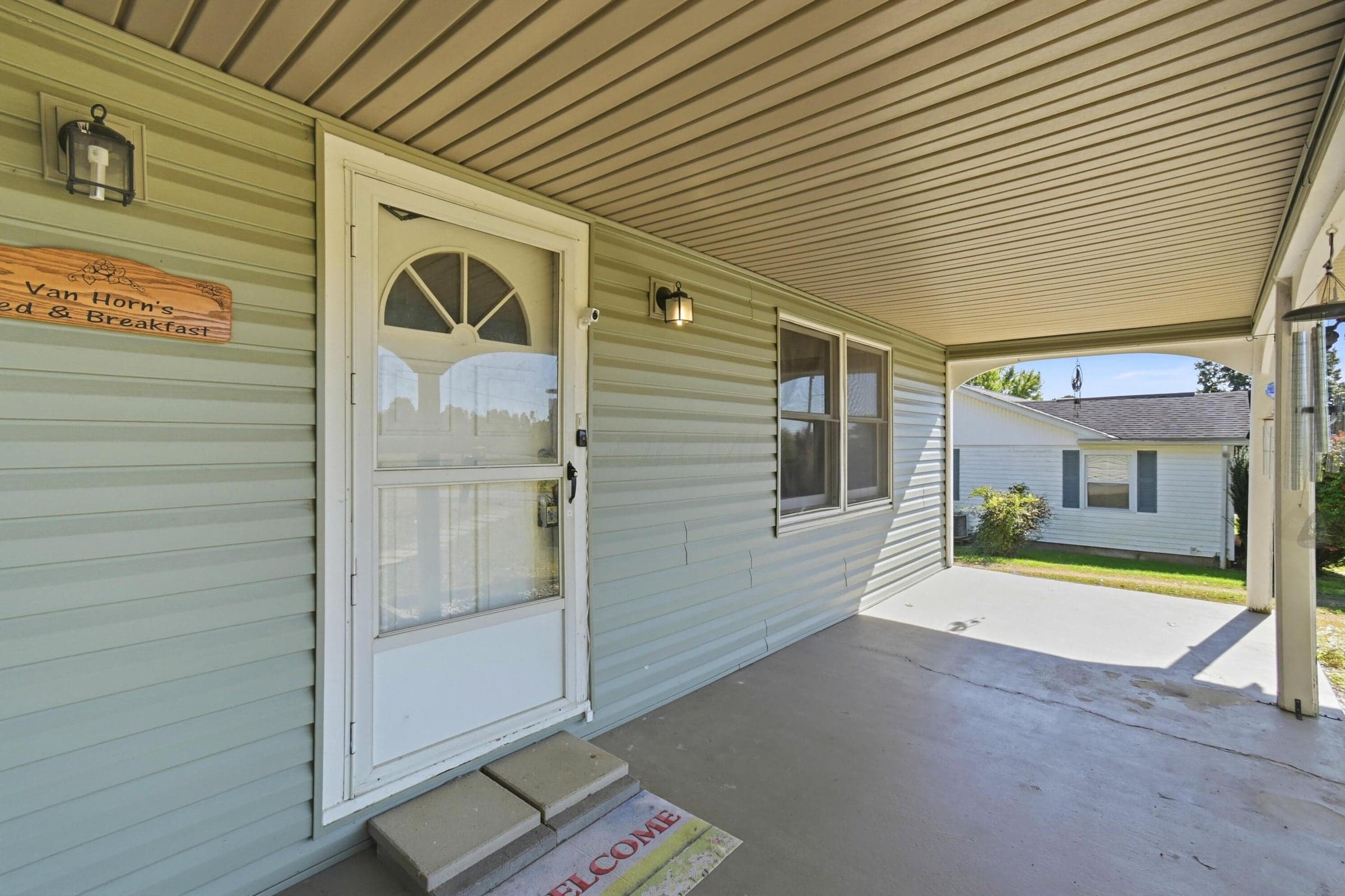 Covered porch entry featuring a storm door, exterior lighting, and siding
