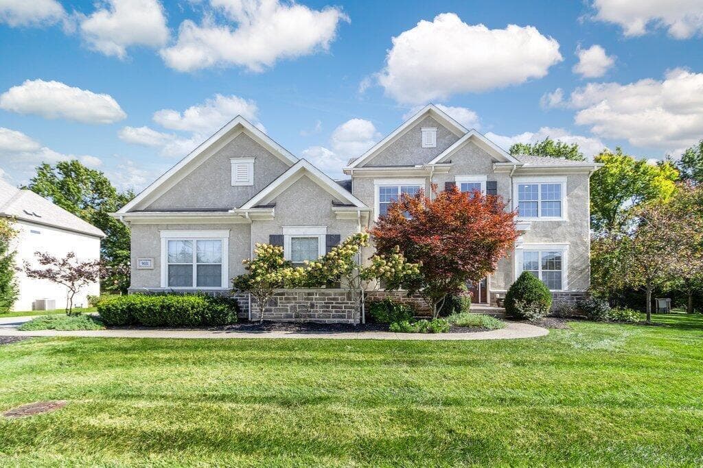 Stucco exterior with stone accenting, multiple gabled rooflines, and a manicured lawn