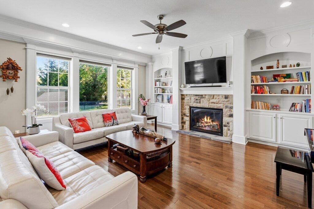 Hardwood flooring, stone-clad fireplace, integrated shelving, and a ceiling fan