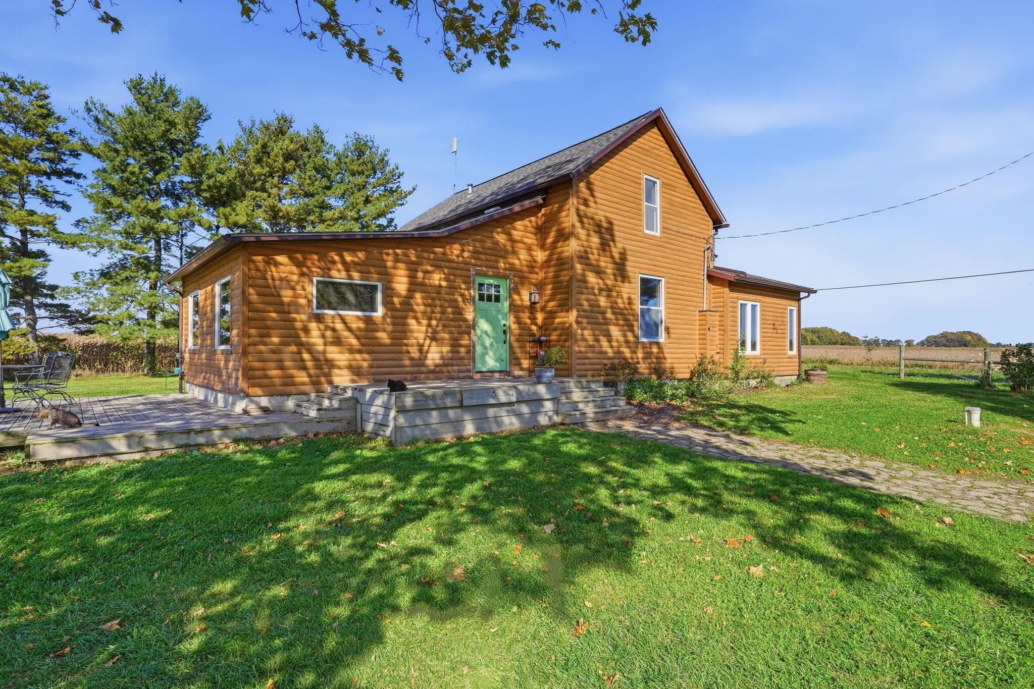 Log cabin exterior featuring horizontal wood siding, a stone-accented front entryway, a concrete paver patio, and mature tree-lined grounds