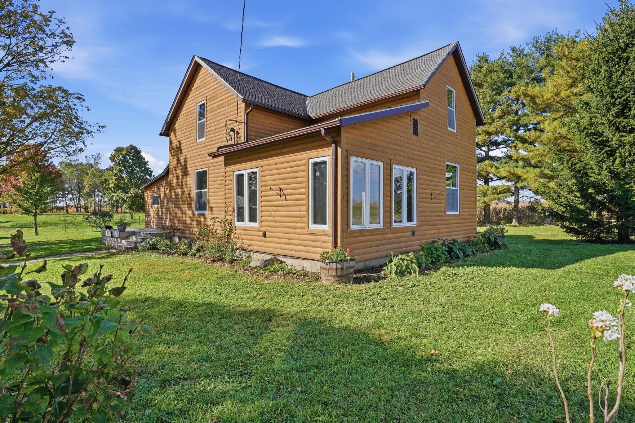 Two-story exterior featuring horizontal wood siding, a gabled roofline, double-hung windows, and a stone-accented foundation