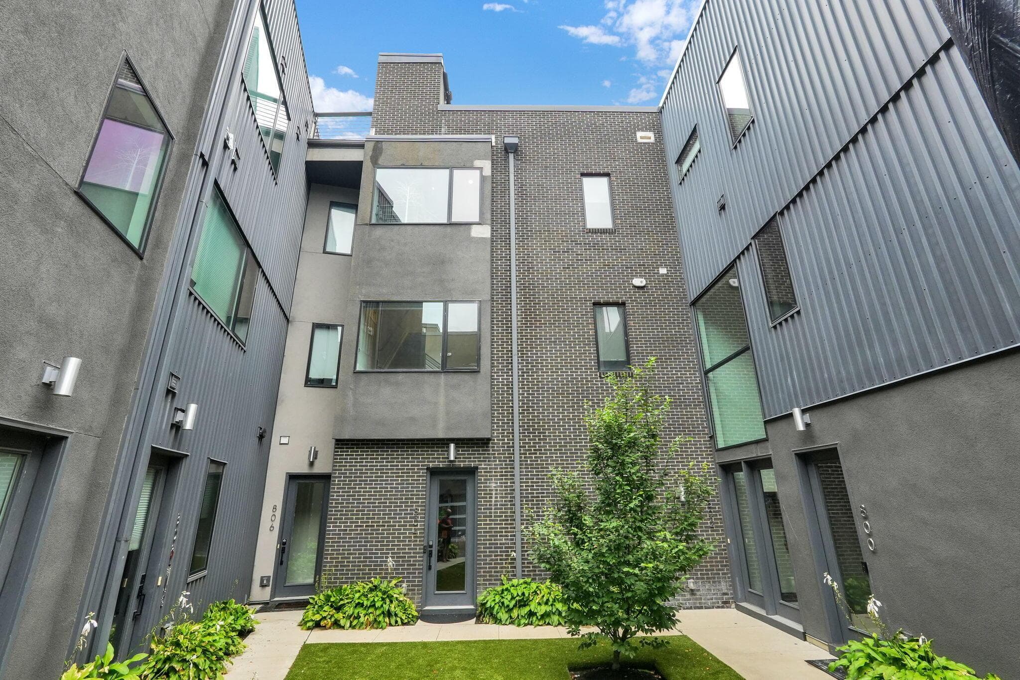 Modern exterior with corrugated metal siding, stucco finish, brick accents,
and a central landscaped courtyard featuring a lawn and plantings