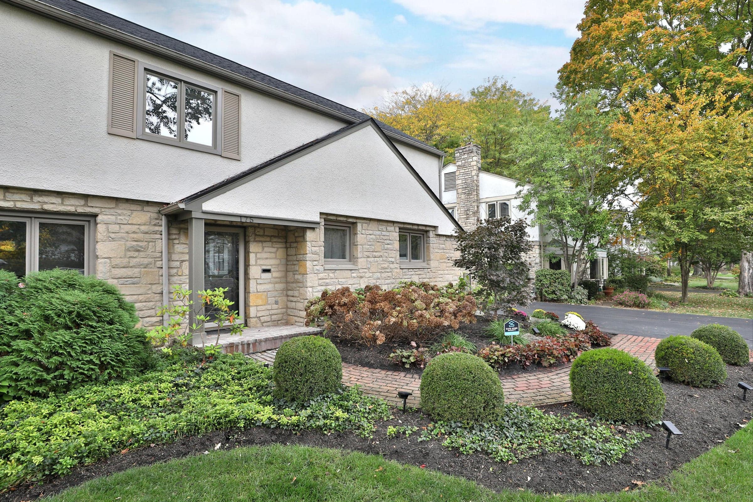 Exterior facade featuring stone masonry, stucco siding, and a brick-accented walkway lined with manicured shrubbery