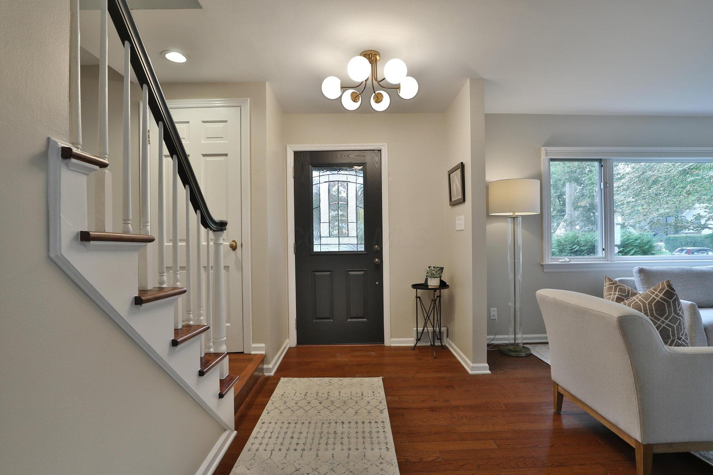 Entryway featuring hardwood floors, a multi-globe chandelier, a front door with a glass inlay, and a staircase with a handrail
