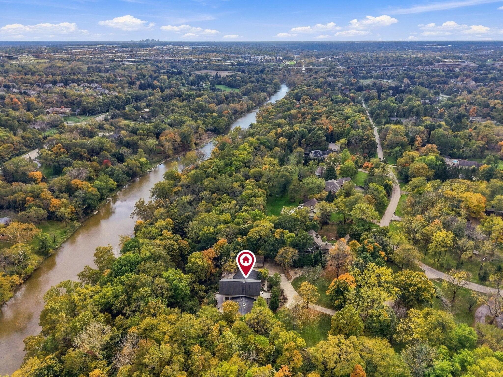 Aerial perspective of a multi-story residence situated on a wooded lot featuring extensive river frontage and dense mature vegetation