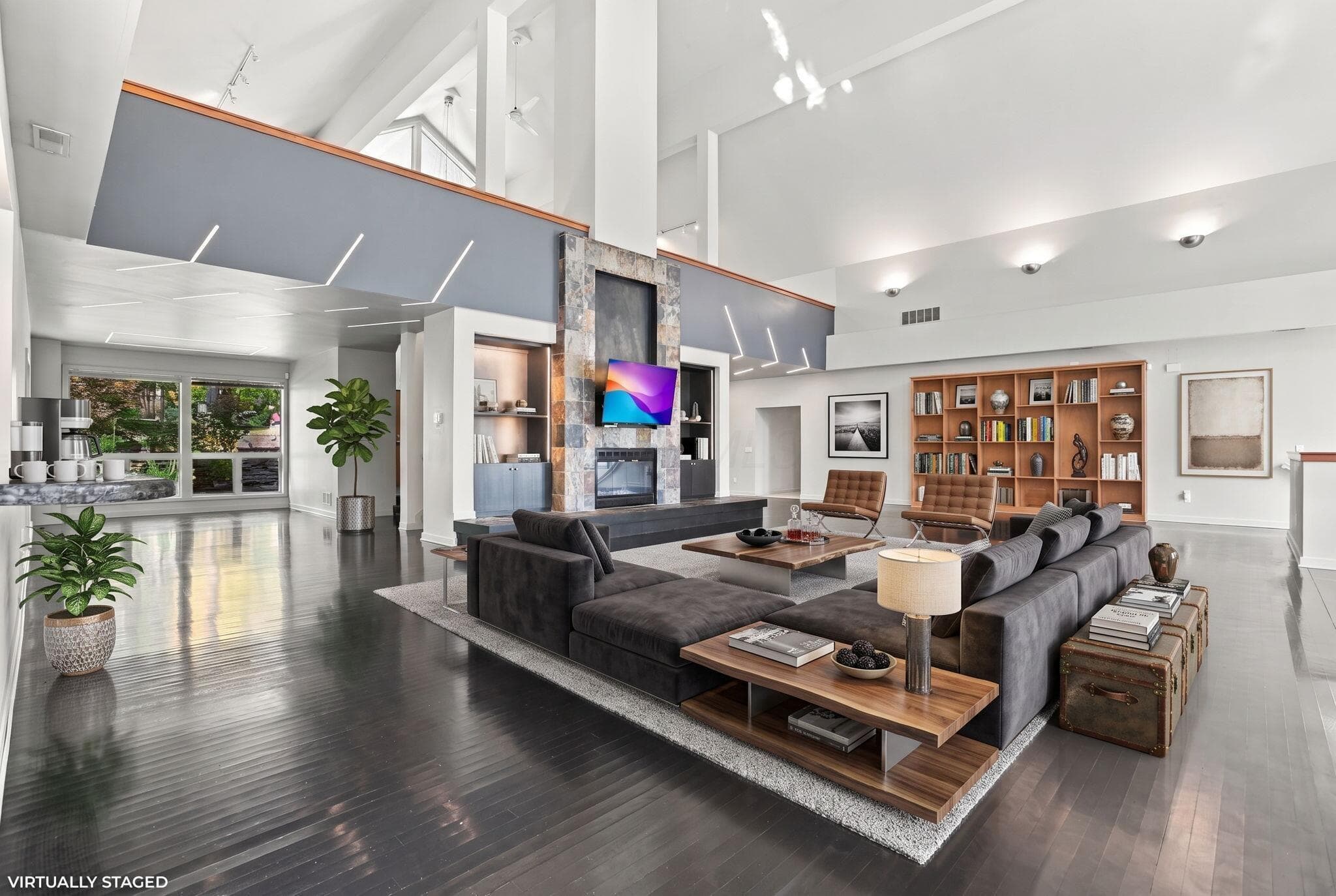 Virtual Staging. Expansive living area featuring vaulted ceilings, floor-to-ceiling stone fireplace, built-in wooden shelving, dark wood-finish flooring, and recessed lighting