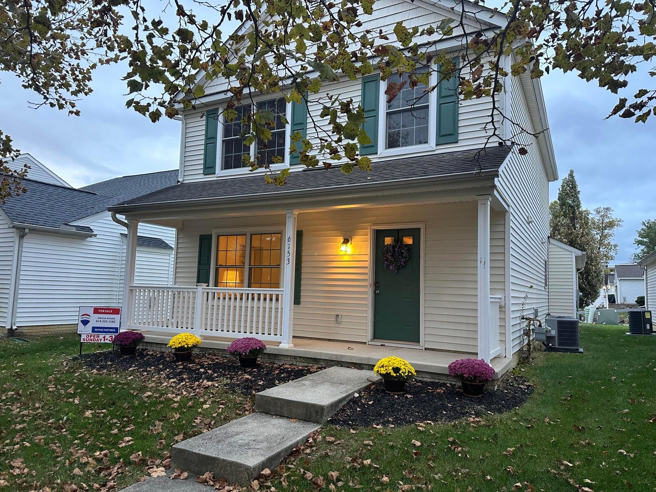 Two-story exterior featuring light-toned vinyl siding, green shutters, and a covered front porch with white railing