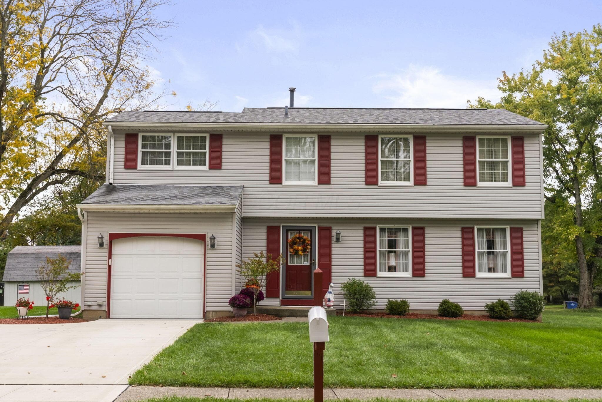 Two-story exterior featuring light-gray horizontal siding, contrasting red shutters, an attached single-car garage, and a concrete driveway