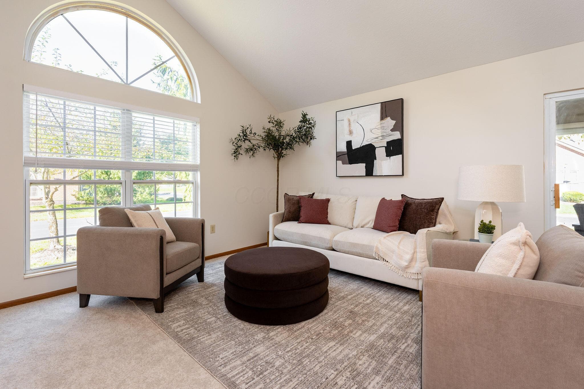 The vaulted Great Room features an arched transom window, large picture window with grid detailing, and newly painted neutral wall tones, complemented by new carpeting.
