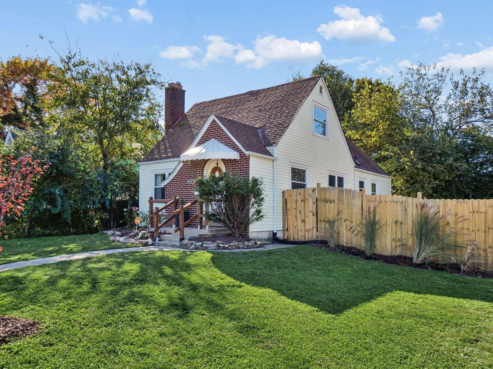 Exterior featuring brick and siding facade, chimney, arched entryway with awning, and wood-panel privacy fencing