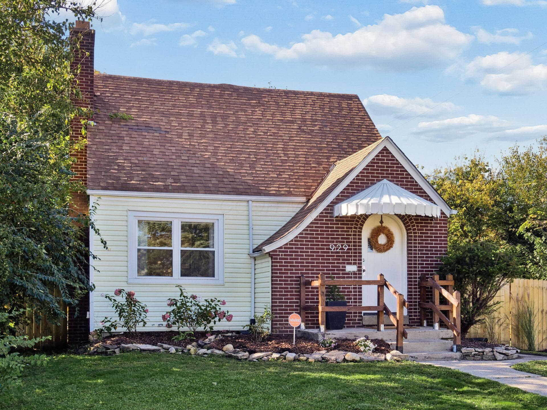 Traditional brick and siding exterior featuring a decorative arched doorway, a scalloped metal awning, a prominent chimney, and stone-bordered landscaping