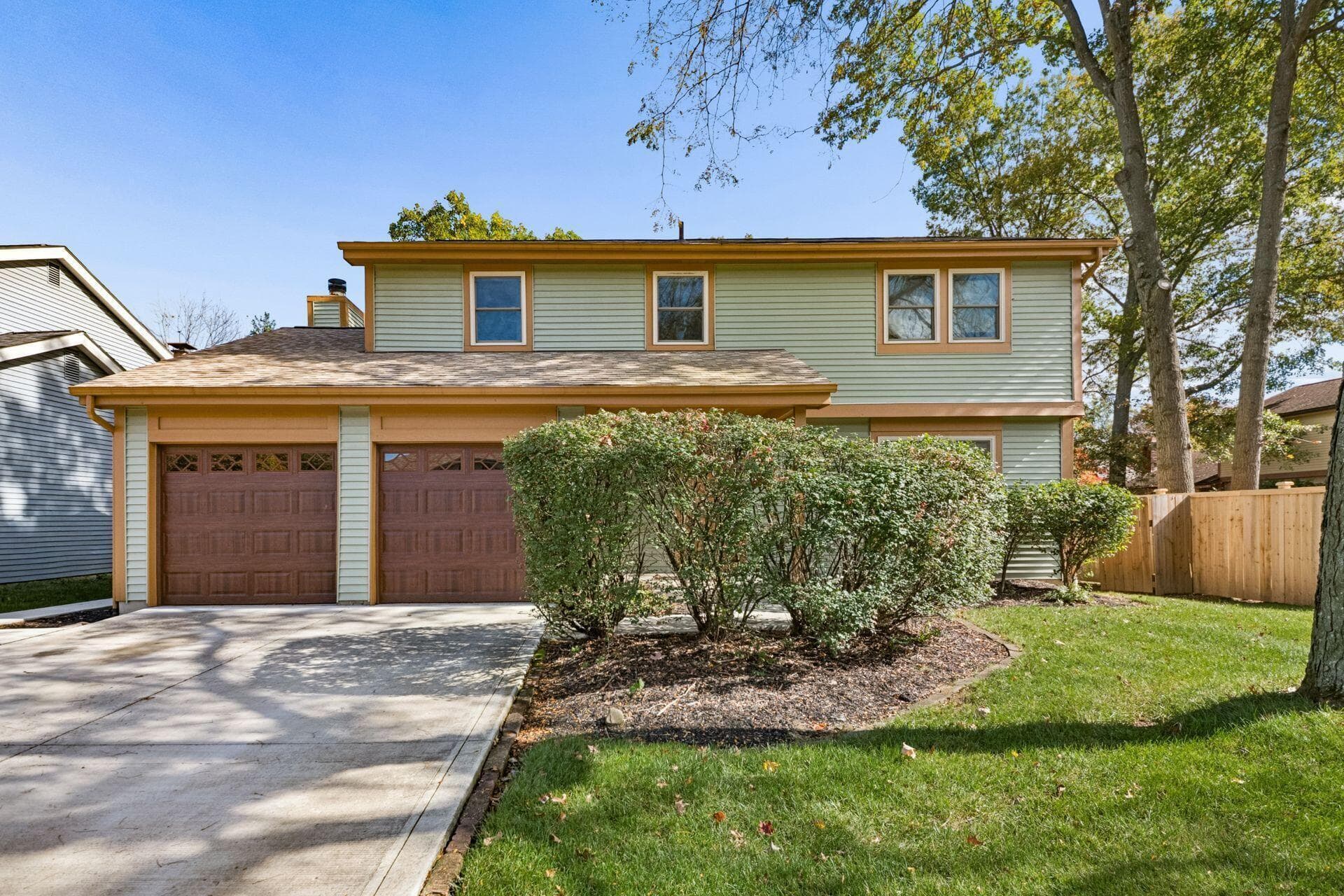 A second view highlights the home's traditional architecture, established landscaping, and spacious driveway.