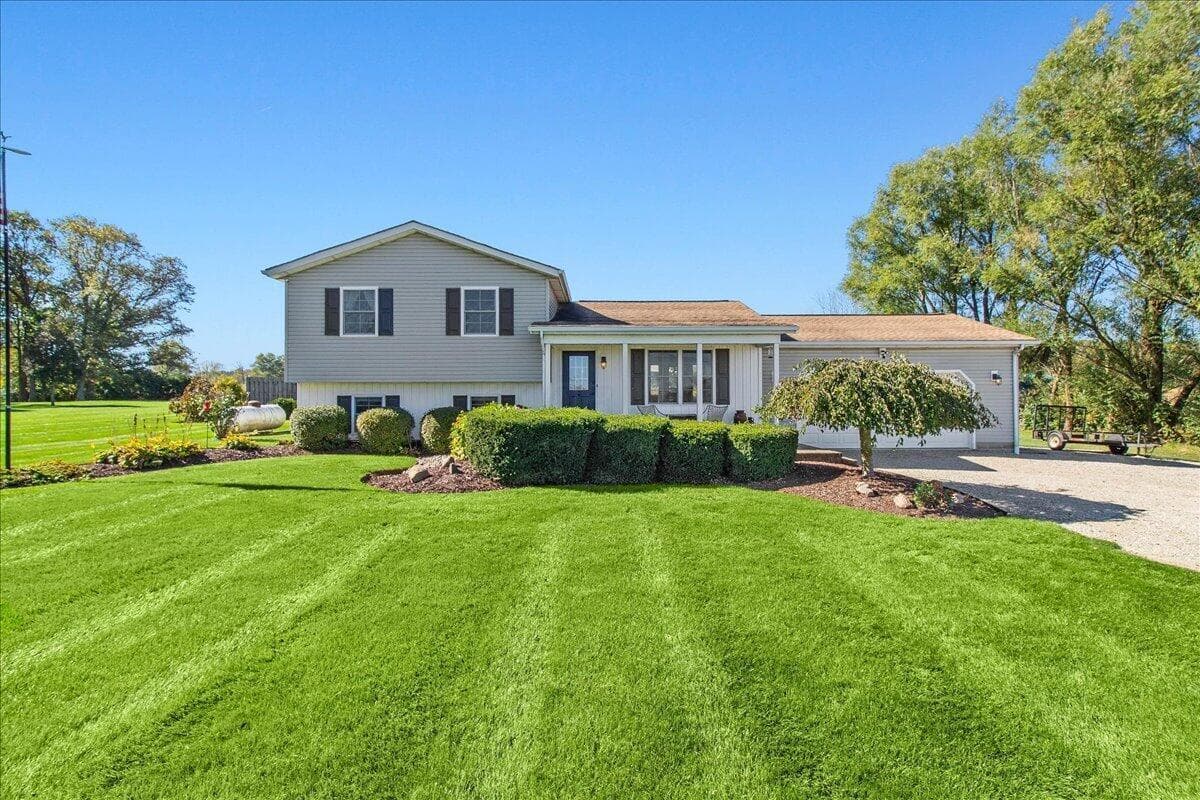 Split-level residence featuring dual-tone exterior siding, dark shutter accents, an attached garage, and landscaped garden beds