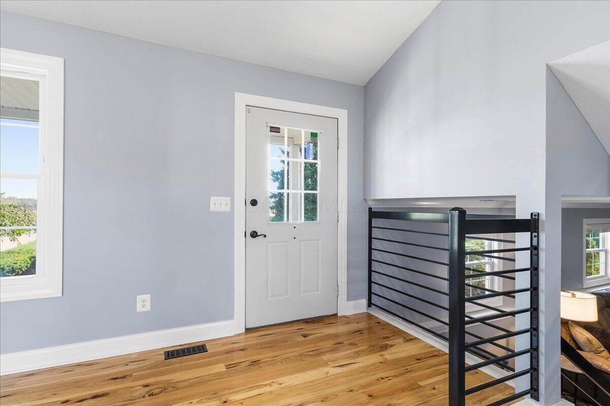 Entryway featuring wood-finish flooring, a six-lite glass panel door, matte black horizontal railing, and vaulted ceilings