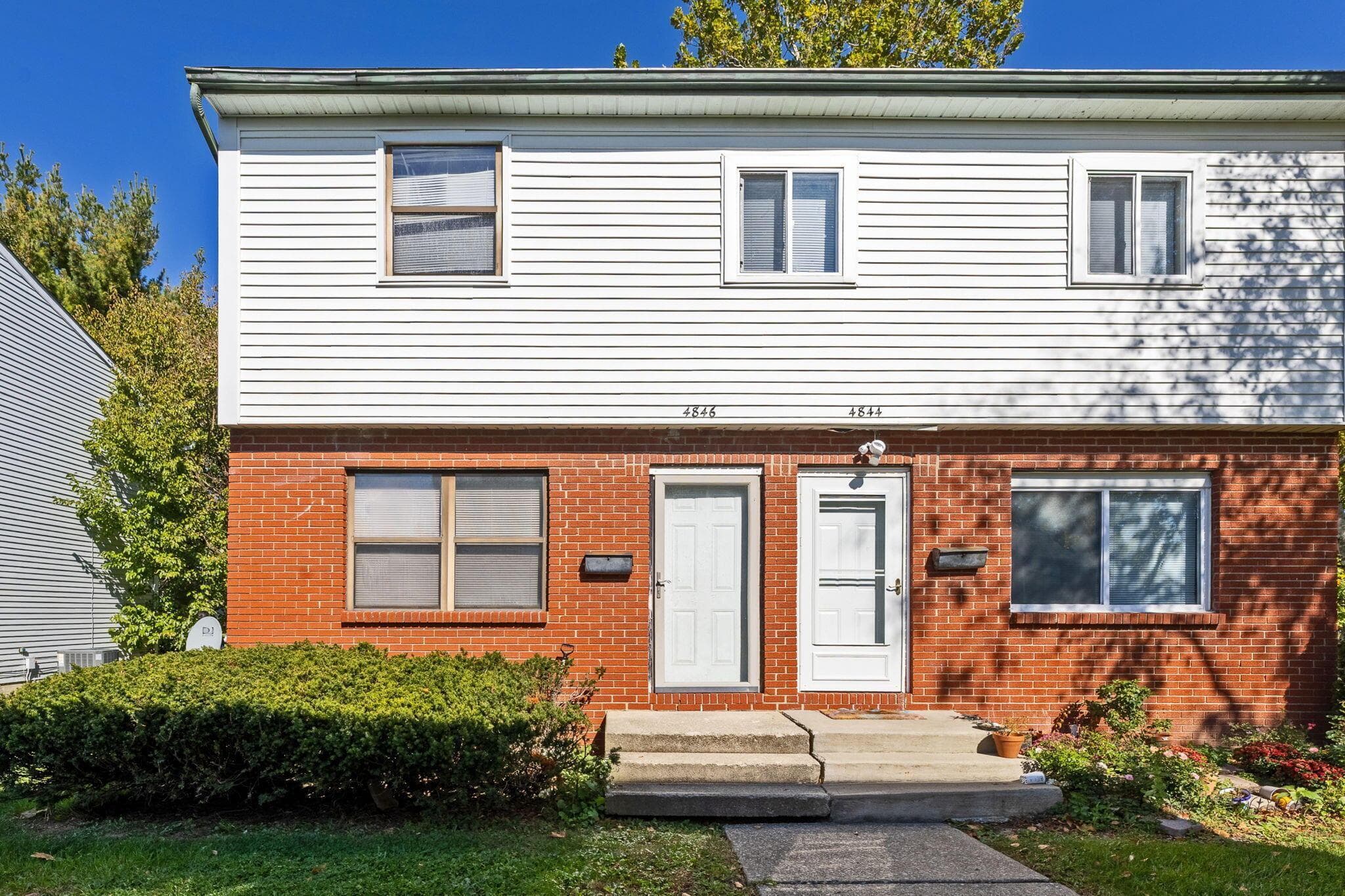 Two-story exterior featuring a brick masonry lower level, white horizontal siding, concrete front steps, and dual entryways