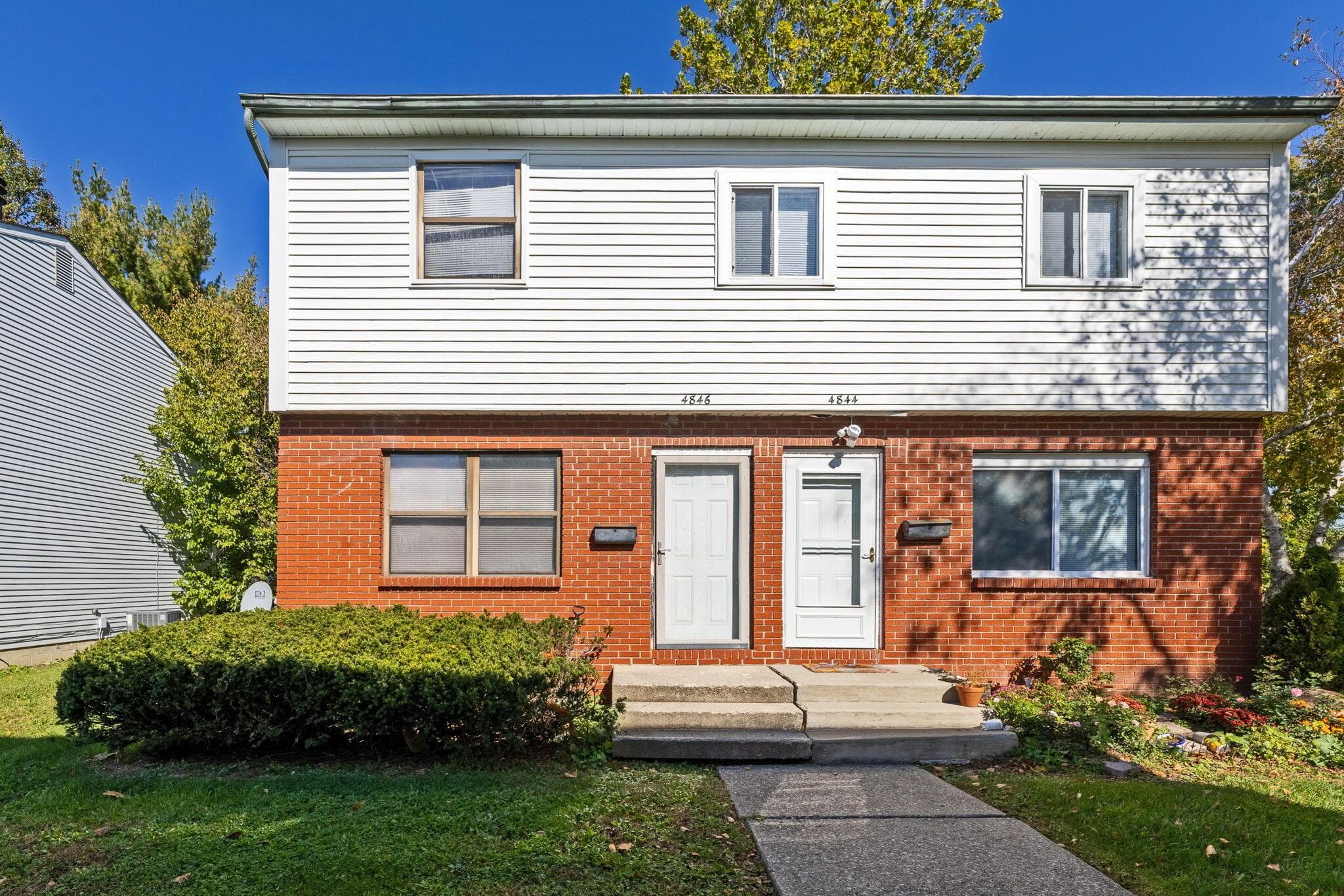 Two-story exterior featuring a brick masonry lower level, horizontal vinyl siding upper level, and dual entrance doors with concrete steps