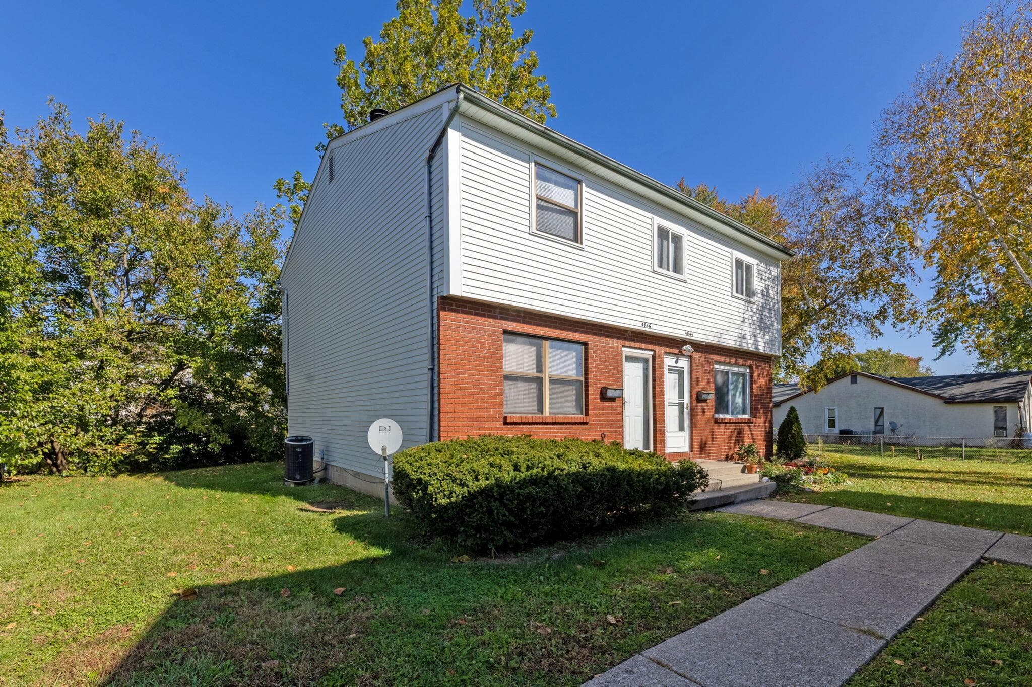 Two-story exterior featuring a brick masonry lower level, white horizontal siding, dual entry doors, and a concrete walkway
