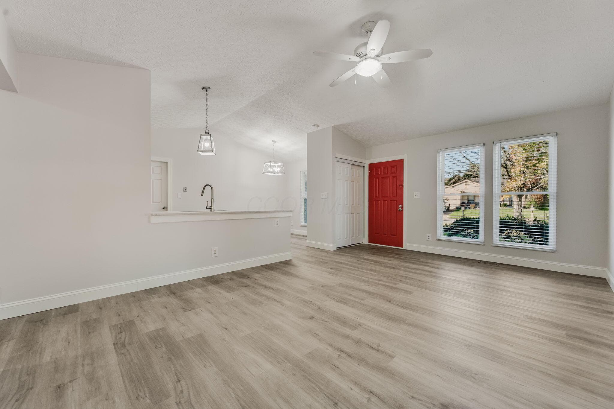Open-concept area featuring wood-finish flooring, vaulted ceilings, a ceiling fan with integrated lighting, dual pendant light fixtures, and a breakfast bar