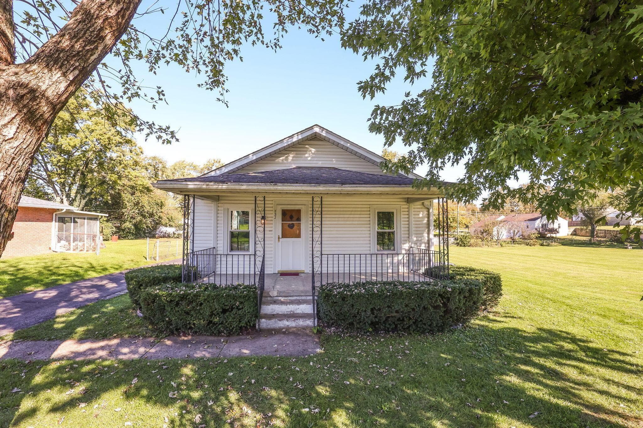 Exterior featuring light-toned horizontal siding, a covered front porch with metal railing, and an expansive lawn