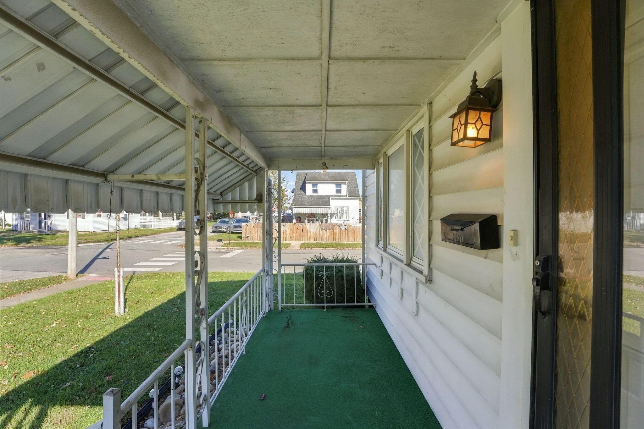 Covered front porch featuring a metal awning, ornamental metal railing, exterior wall-mounted lantern-style lighting, and a metal mailbox