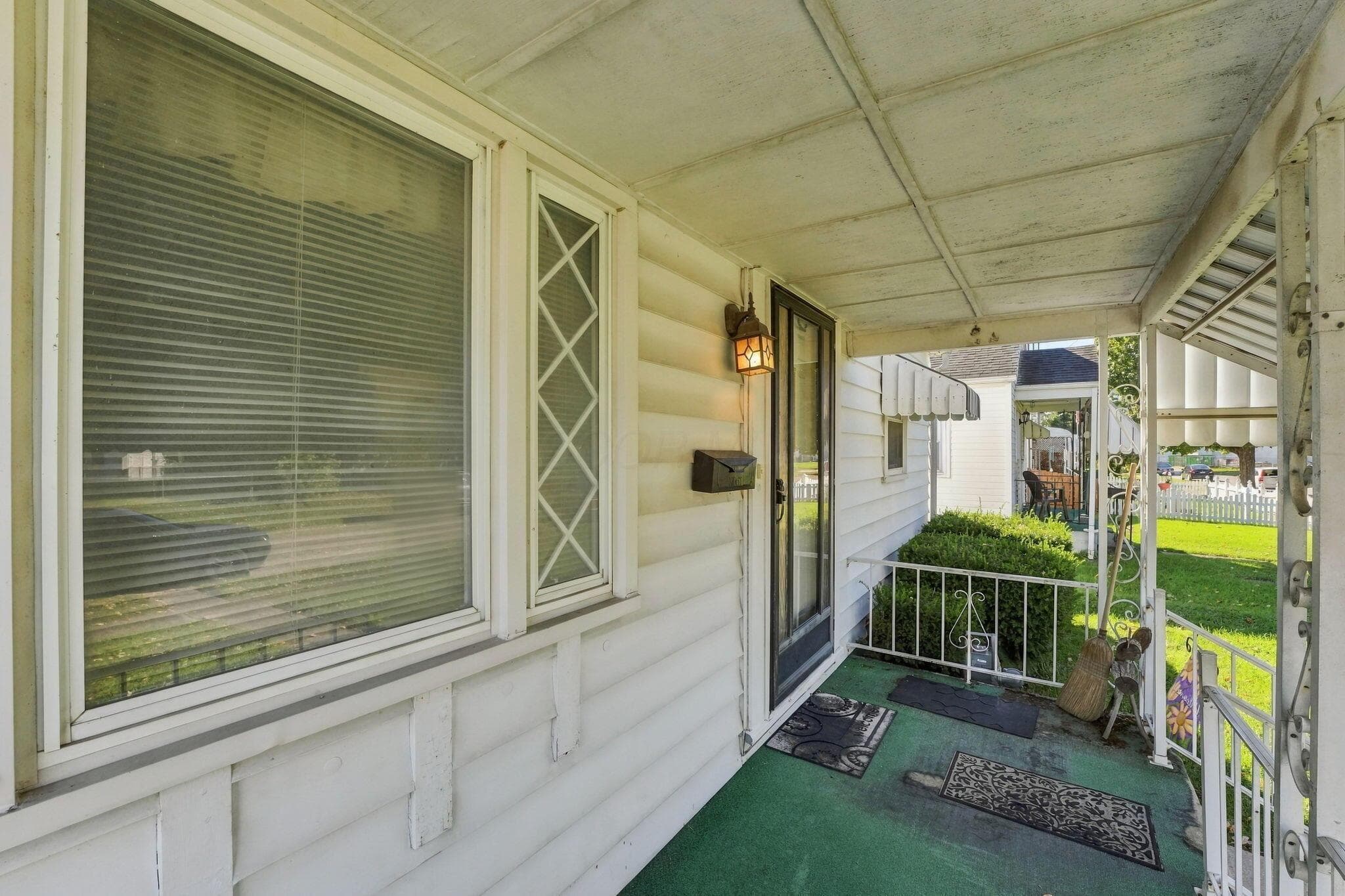 Covered front porch featuring white horizontal siding, diamond-pattern window muntins, and a wall-mounted lantern-style exterior light fixture