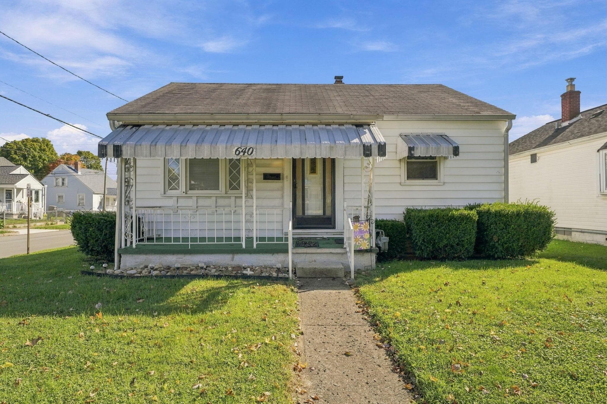 Single-story residence featuring horizontal lap siding, a covered front porch with decorative metal railings, metal window awnings, and a gabled roof