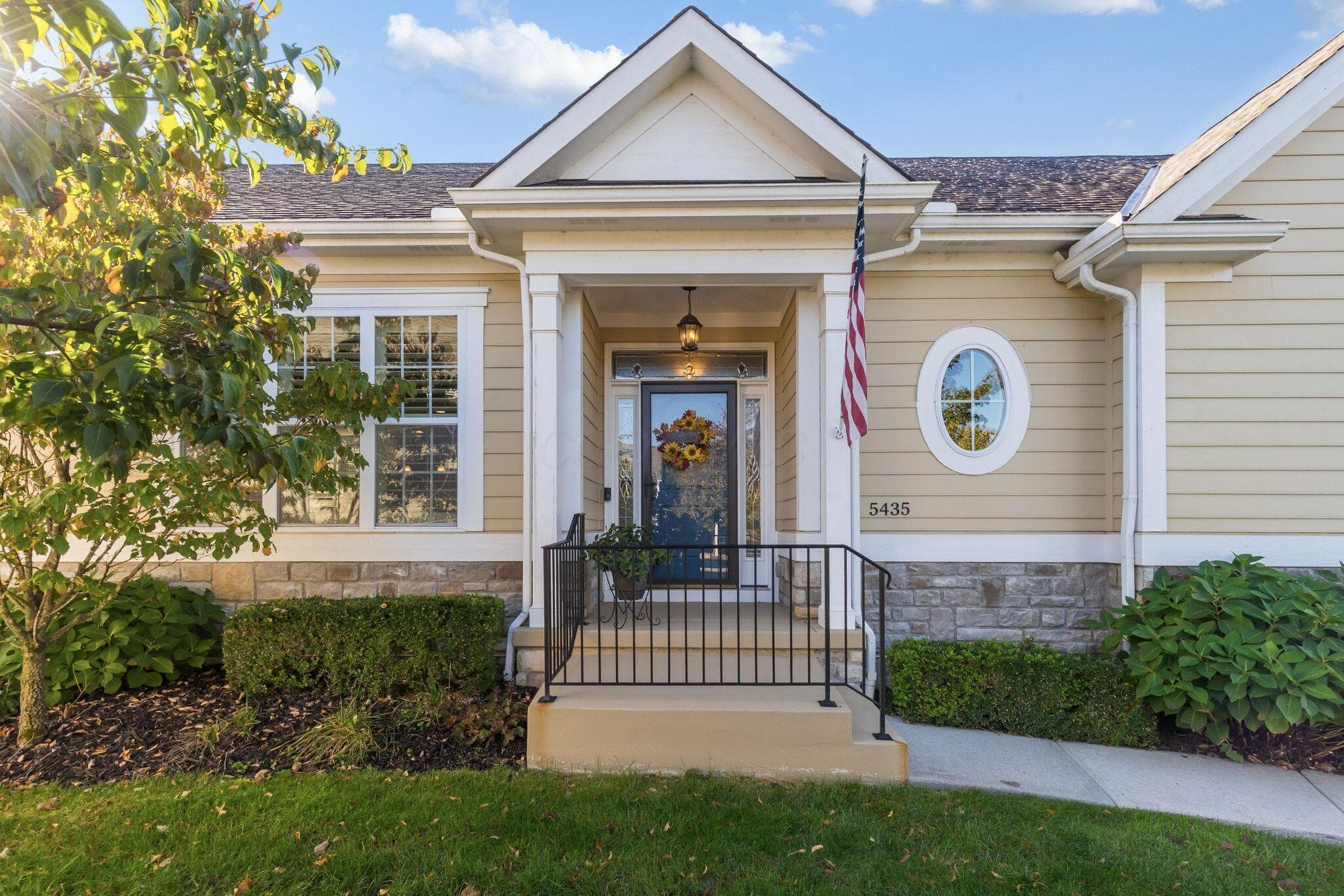 Exterior facade featuring lap siding, stone veneer accents, a covered front entryway with a gabled roofline, an oval accent window, and a metal railing